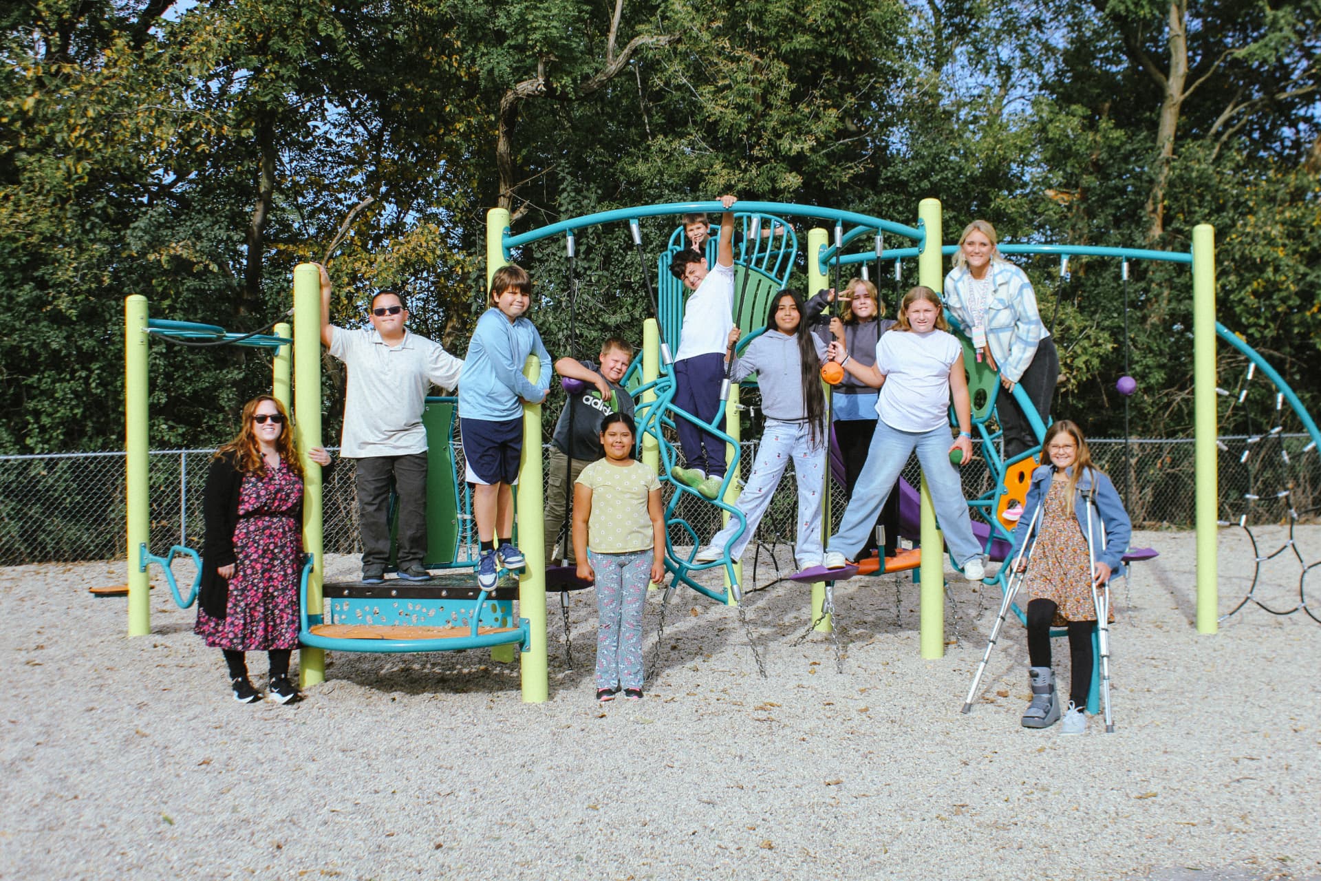 A group of smiling St. Mary students and two teachers pose together on a colorful outdoor playground climber