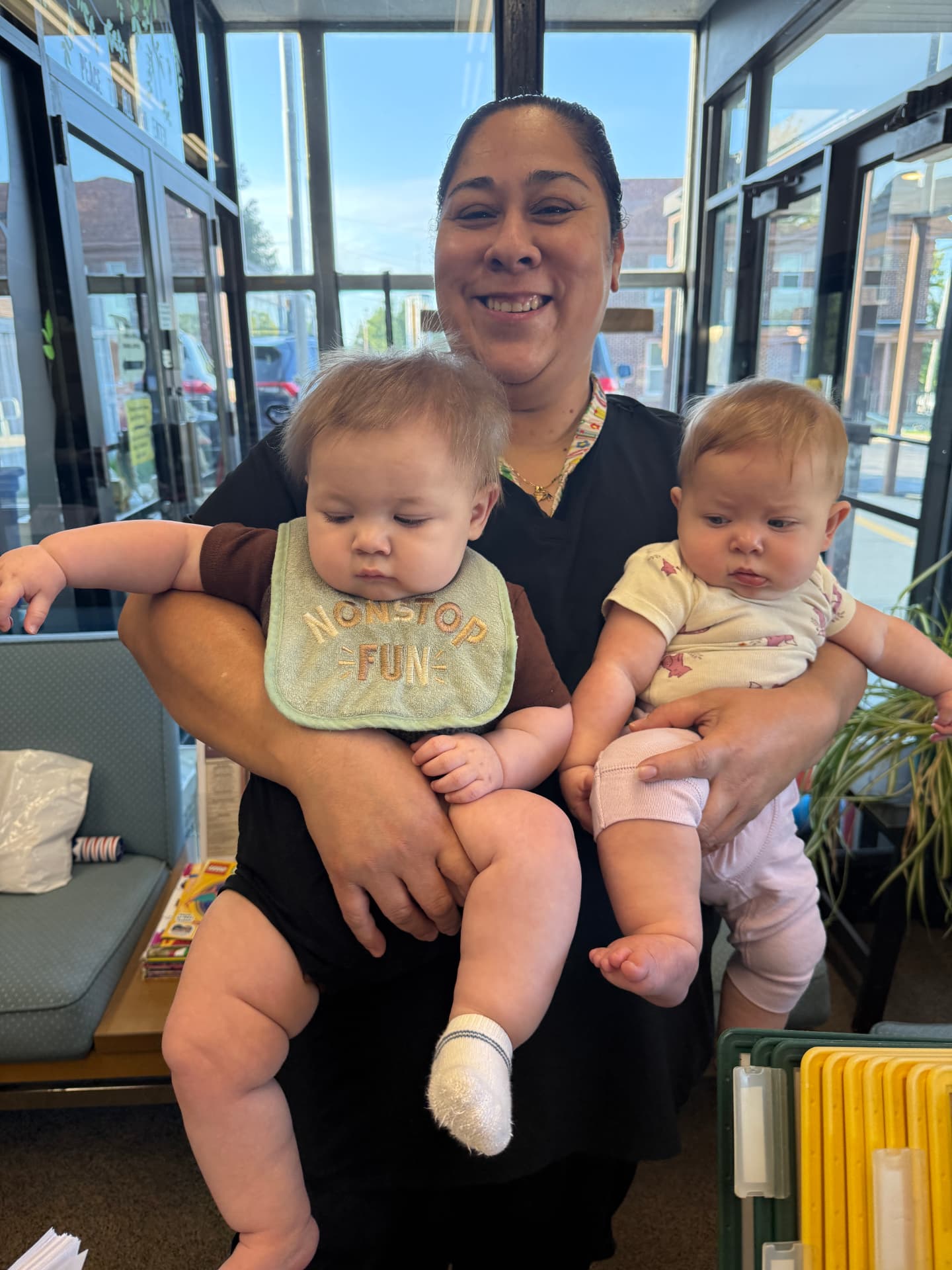 A caregiver smiles while holding a baby in each arm just inside the school entryway