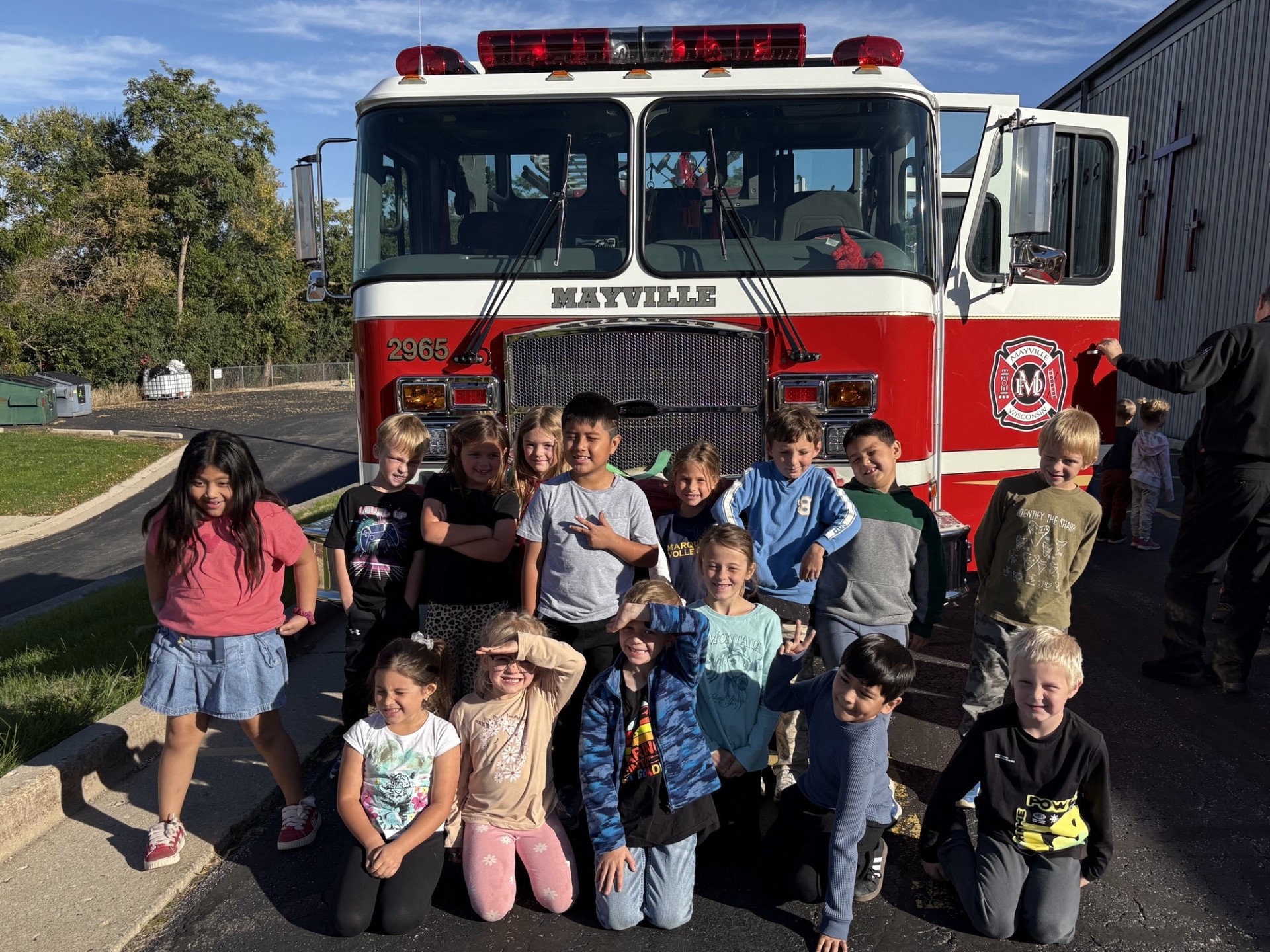 A class of students poses in two rows in front of a Mayville fire department engine